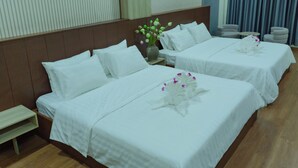 A hotel room with two beds, a small table, and a vase of flowers. - Peaceful Hotel (Vientiane)