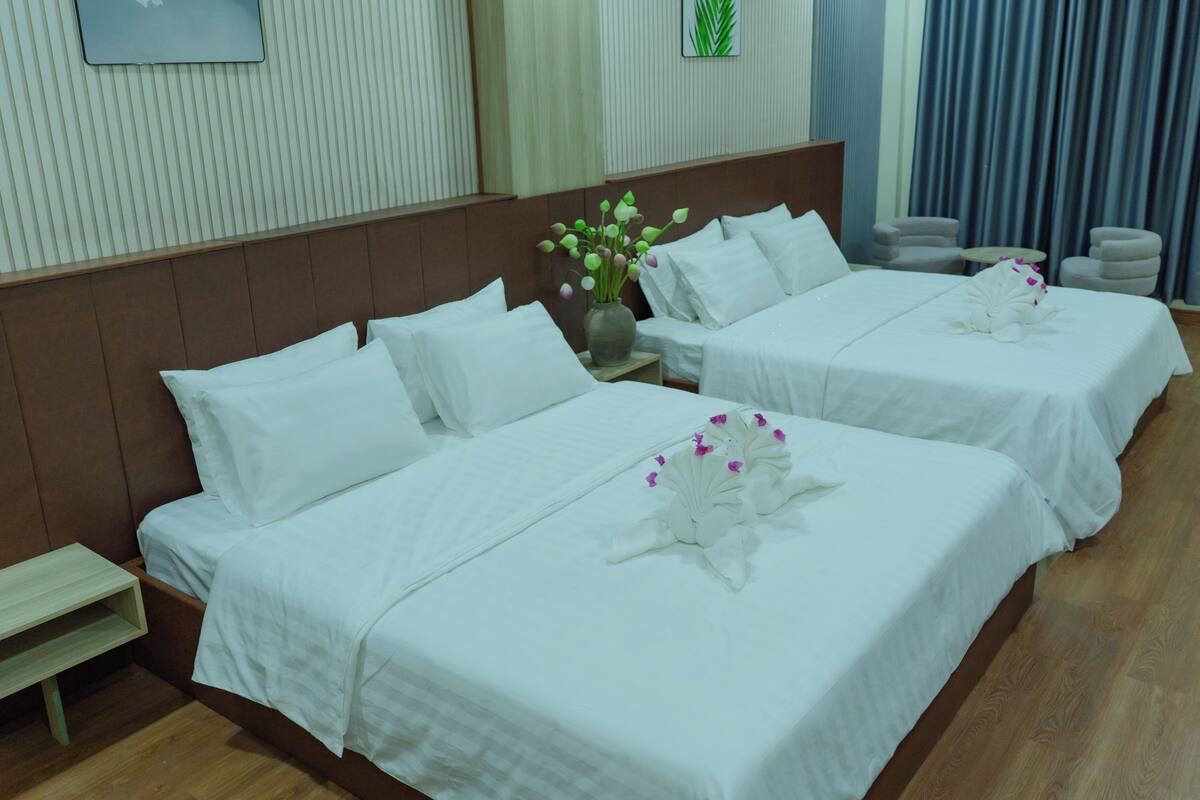 A hotel room with two beds, a small table, and a vase of flowers.