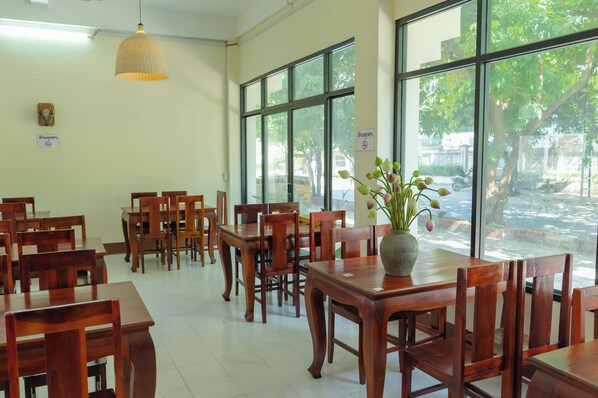 Un ristorante con tavoli e sedie in legno, ampie finestre e un lampadario.