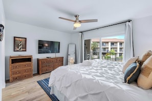 A bedroom with a bed, a ceiling fan, a TV, wooden furniture, and a balcony with a view. - Ohana Bliss l 2 Pools l Walk to Beach (St. Augustine Beach)