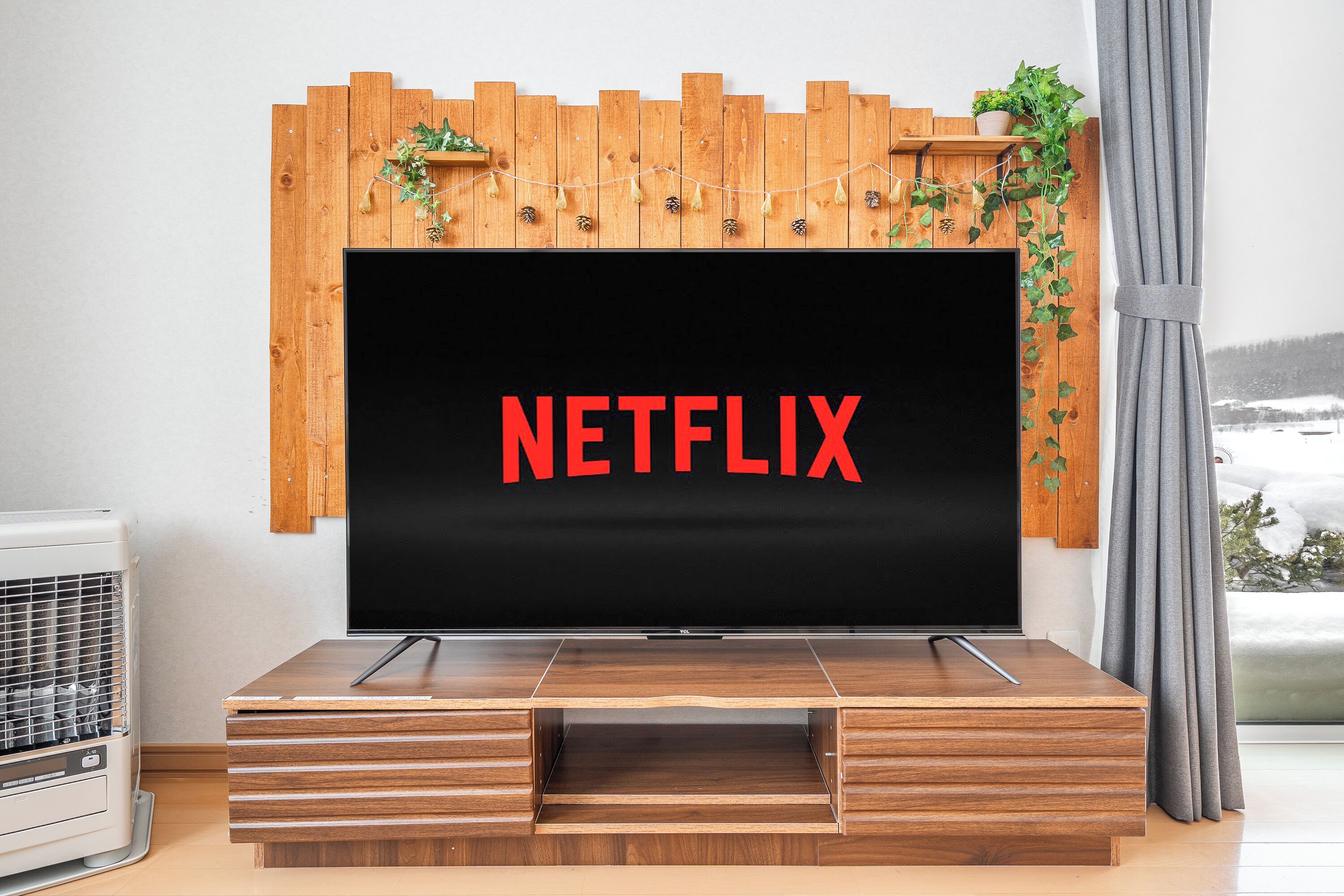 A modern living room with a flat-screen TV mounted on a wooden wall, a built-in entertainment unit below, and a view of a snowy landscape through a window.