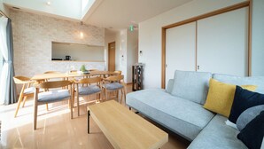 A modern living room with a sofa, a coffee table, and a dining area with chairs and a table. - CLEMATIS (Nakafurano)
