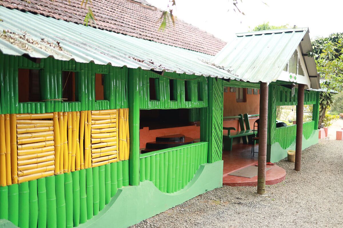 A green building with a corrugated metal roof, a covered outdoor seating area, and a gravel ground.