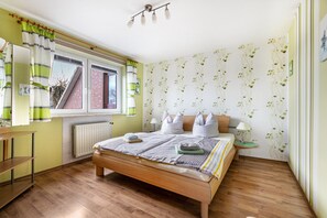 Et soveværelse med en træseng, et vindue med gardiner, en radiator og en væg med blomsteret tapet.