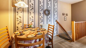 Un coin repas avec un papier peint à rayures, une table ronde dressée pour quatre personnes et une chaise en bois.