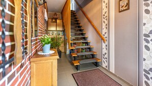 Un escalier avec des marches en bois et une rampe, menant à un palier où se trouvent un pot de fleurs et une petite table.