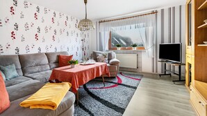 Un salon moderne avec un canapé, une table à manger, un téléviseur et une vue sur un bâtiment à l’extérieur.