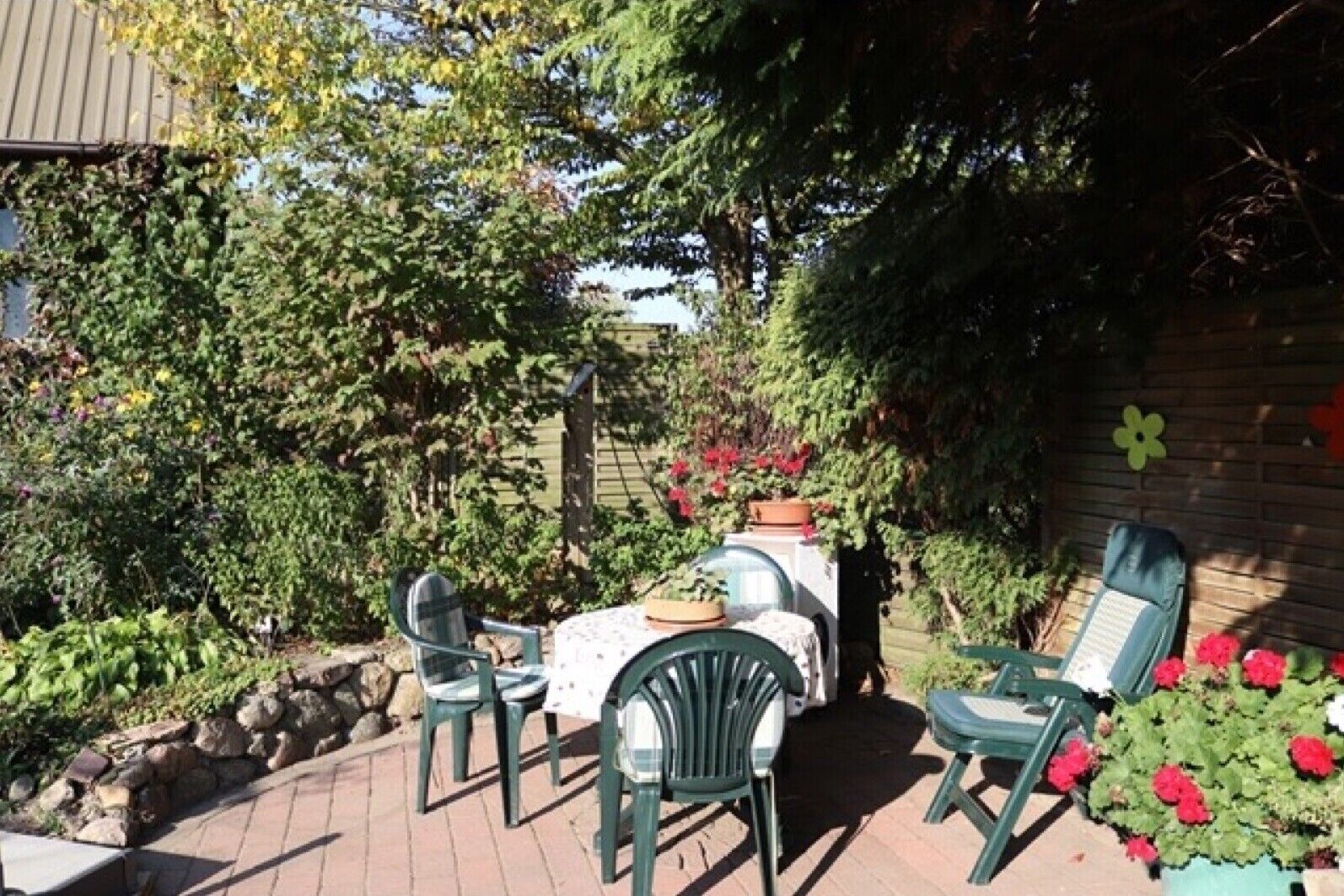 A patio area with a table and chairs, surrounded by plants and a wooden fence.
