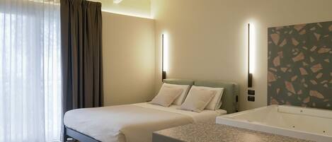 A hotel room with a bed, a small sofa, a bathtub, and a large window with curtains.