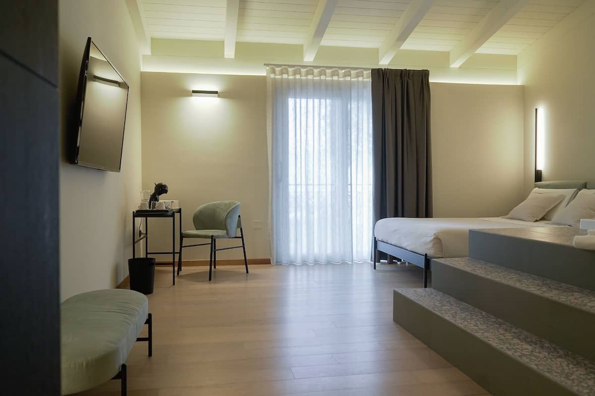A hotel room with a bed, a chair, a desk, and a large window with curtains.