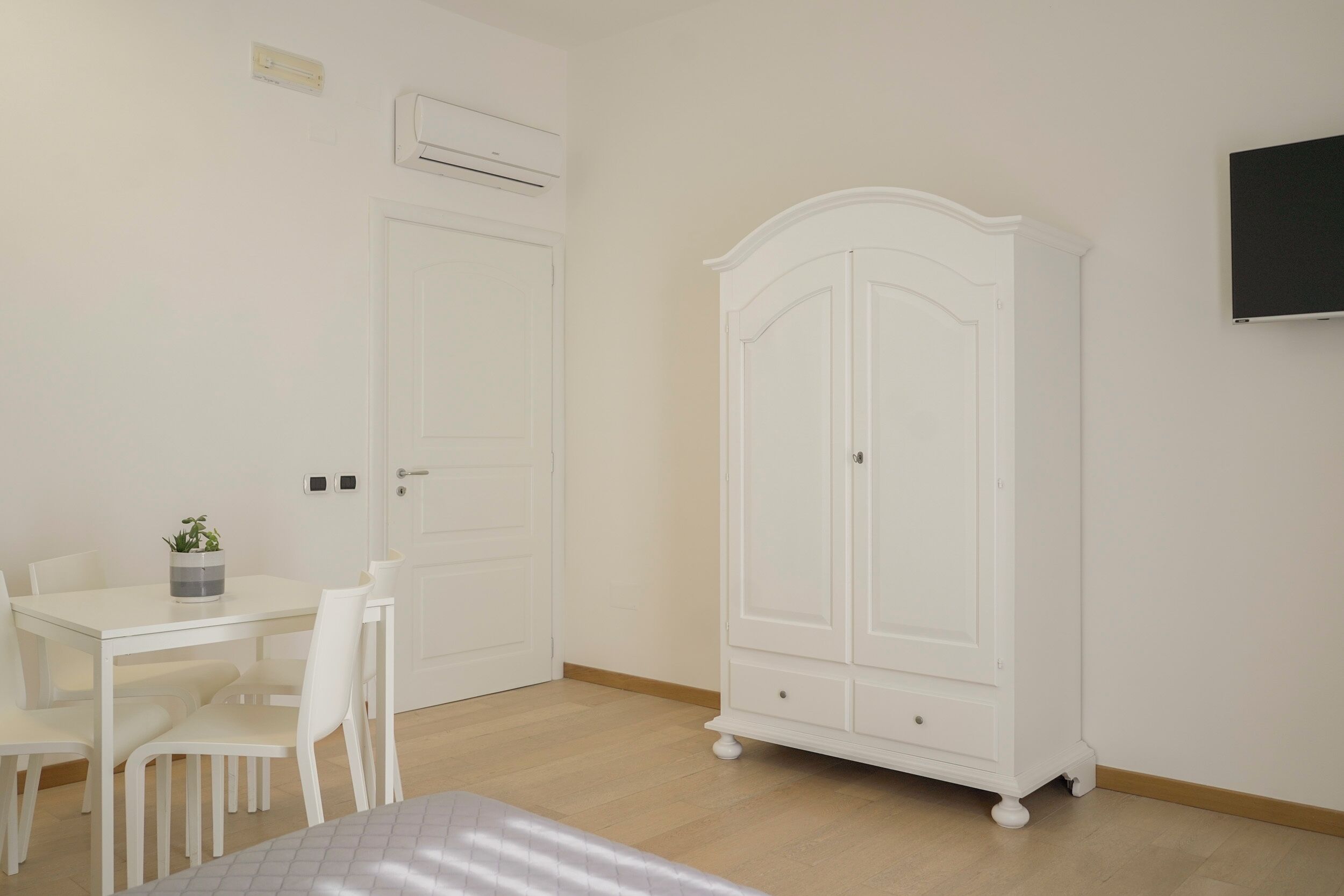 A room with a white wardrobe, a white table with chairs, and a bed.