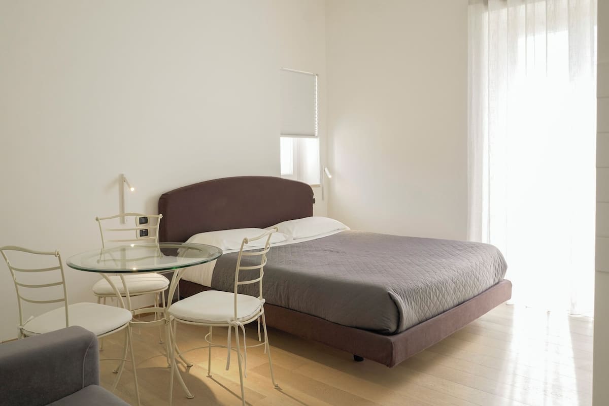 A bedroom with a bed, a glass table, two chairs, and a bedside table.