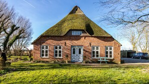 A brick house with a thatched roof, a front door, and a bench outside. - Holiday Apartment 'Reetdachhof Familie Dührsen' with Shared Terrace, Shared Garden and Wi-Fi (Norddeich)