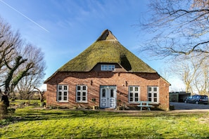 A brick house with a thatched roof, a front door, and a bench outside.