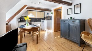 A kitchen with wooden beams, a dining table with chairs, a cabinet, and a wicker chair. - Holiday Apartment 'Reetdachhof Familie Dührsen' with Shared Terrace, Shared Garden and Wi-Fi (Norddeich)
