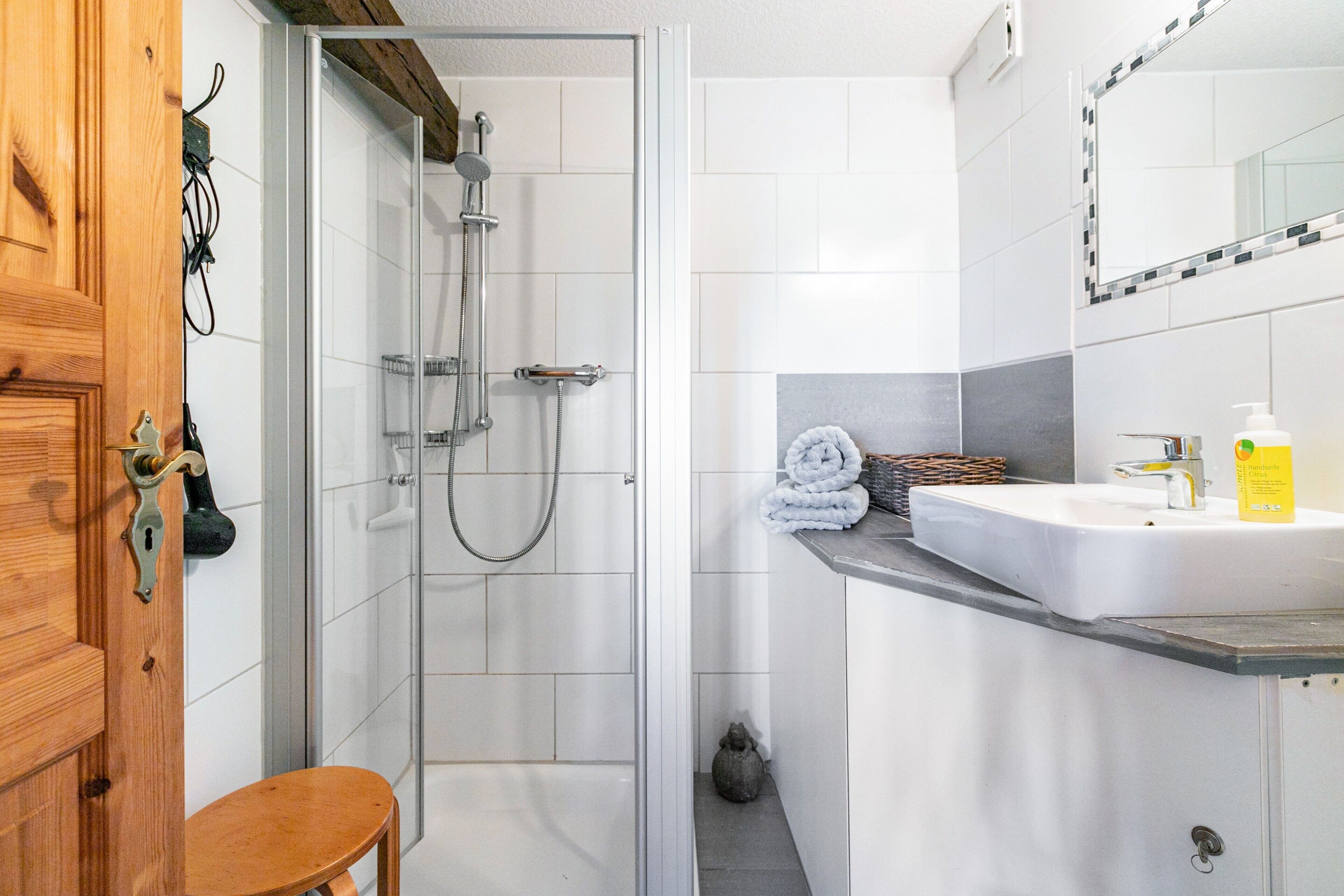 A bathroom with a shower, a sink, and a wooden door.