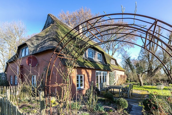 A house with a thatched roof, a brick exterior, and a garden with a wooden bench and table.