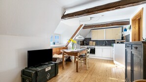 A loft-style living space with a wooden floor, a dining area, a kitchen with white cabinets, and a television. - Holiday Apartment 'Reetdachhof Familie Dührsen' with Shared Terrace, Shared Garden and Wi-Fi (Norddeich)