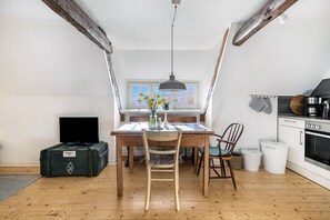 Un espace repas comprenant une table, des chaises, un téléviseur et, au fond, une cuisine.