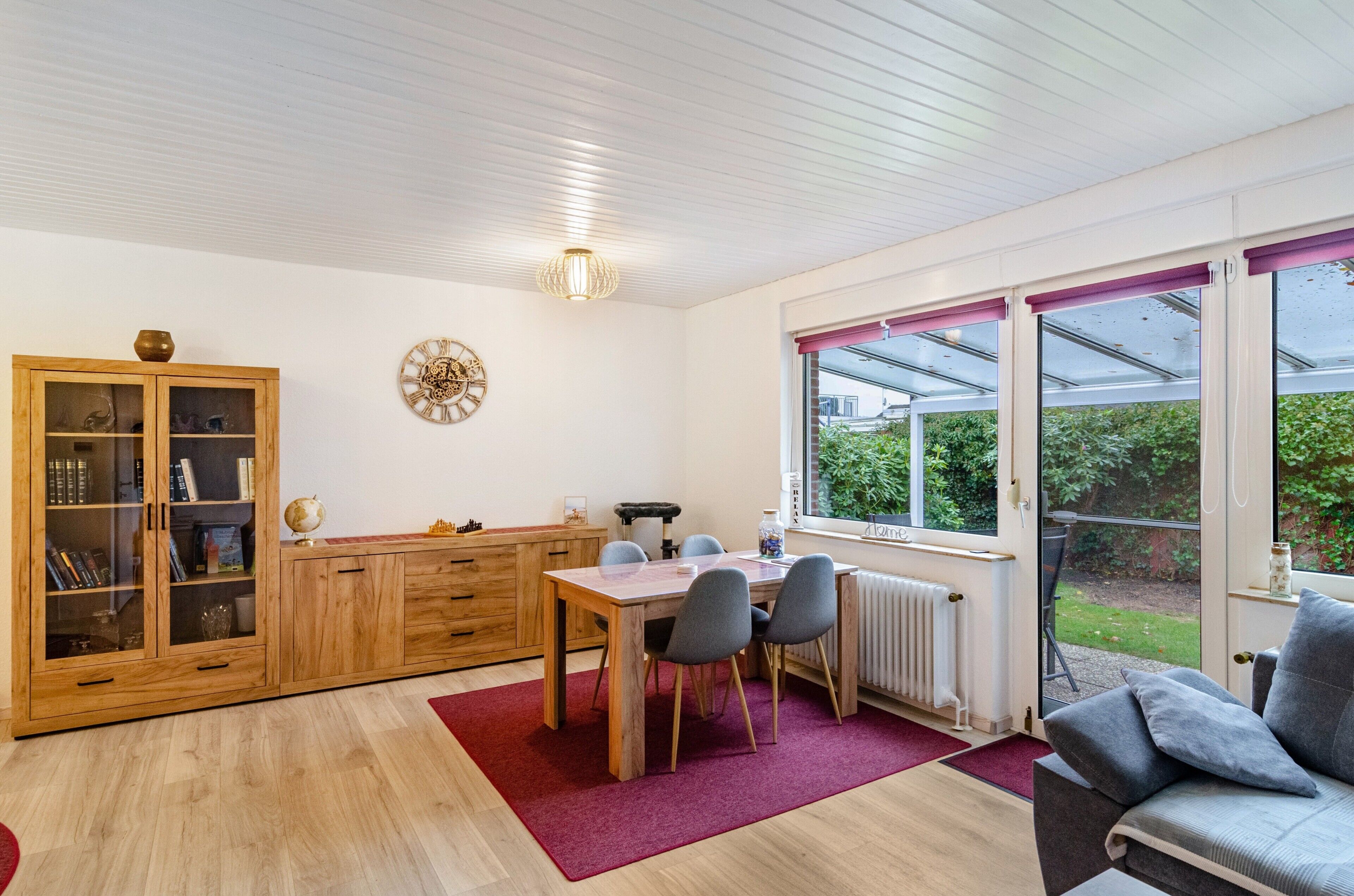 Une pièce comprenant un meuble en bois, une table à manger avec des chaises, un radiateur et une fenêtre donnant sur un paysage verdoyant.