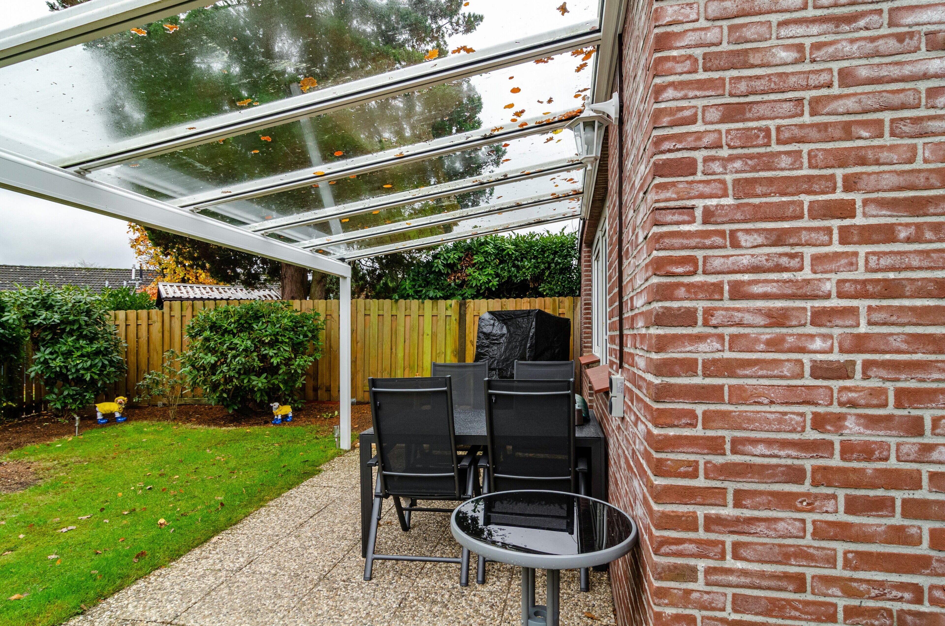 Un patio techado con pared de ladrillo, cerca de madera y un pequeño jardín.