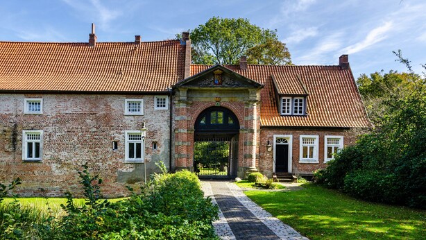 A brick building with a red-tiled roof, a central archway, and a paved pathway leading to the entrance. - Bungalow 'Perle von Berumbur' with Private Terrace, Private Garden and Wi-Fi (Berumbur)