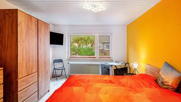 Ett sovrum med en säng, ett skrivbord, en stol, en garderob, ett element och ett fönster med utsikt över grönområden.