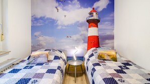 A bedroom with two beds, a nightstand, a lamp, and a mural of a lighthouse. - Bungalow 'Perle von Berumbur' with Private Terrace, Private Garden and Wi-Fi (Berumbur)