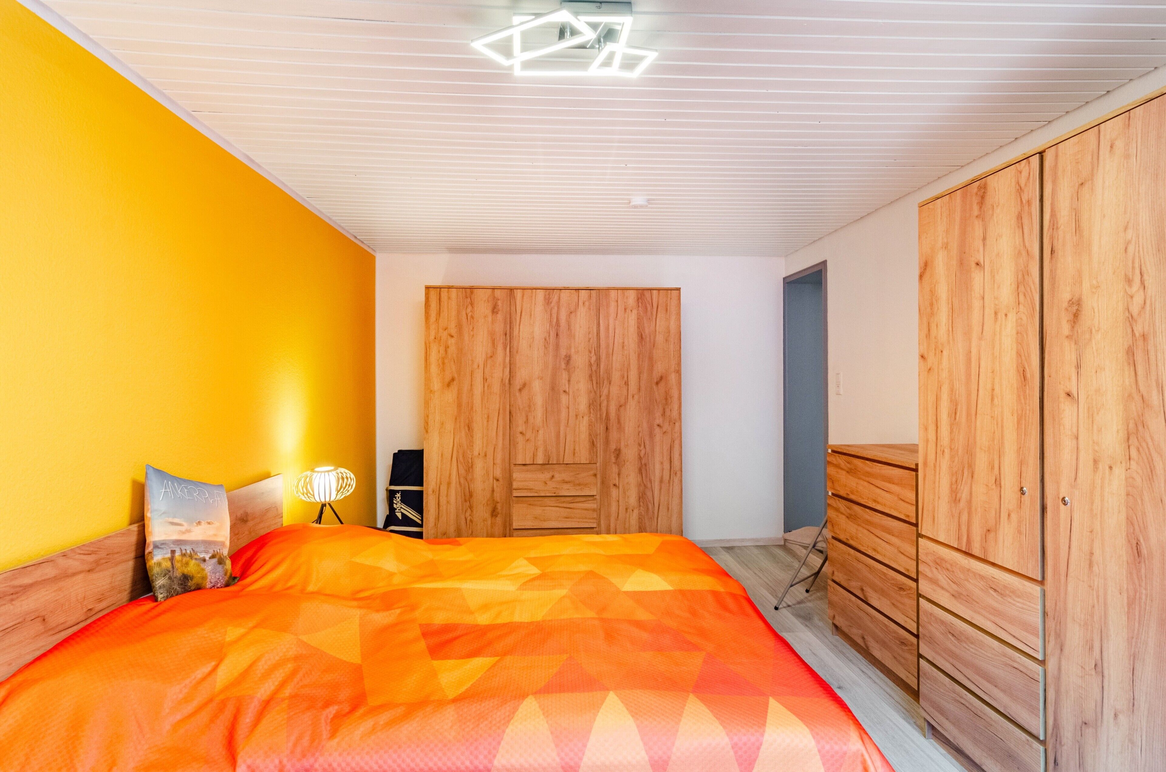 A bedroom with a bed, wooden wardrobe, and a nightstand with a lamp.