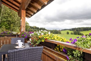 A wooden deck with wicker chairs and a table, overlooking a lush green landscape with a wooden railing adorned with flowers. - Holiday Apartment 'Sonnenstrahl' with Shared Garden, Balcony and Wi-Fi (Friesenried)