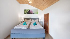 A bedroom with a wooden ceiling, a bed with two pillows, a nightstand with a lamp, and a door.