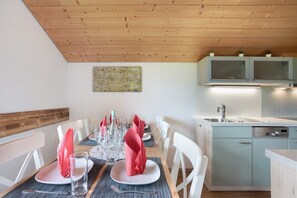 Et spiseområde med træloft, hvide stole og et bord dækket med tallerkener, glas og røde servietter.