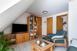 Una sala de estar con televisor, estanterías de madera, un sofá verde y una mesa de centro.