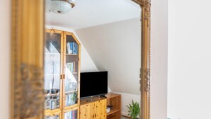 A living room with a wooden bookshelf, a flat-screen TV, and a small plant. - Apartment 'Fewo- Nommensen' with Shared Garden and Wi-Fi (Oland)