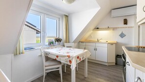 A kitchen with a dining table, white cabinets, a window with curtains, and a small sink. - Apartment 'Fewo- Nommensen' with Shared Garden and Wi-Fi (Oland)