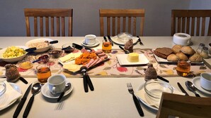 A dining table set with various breakfast items, utensils, and a patterned tablecloth. - Apartment 'Fewo- Nommensen' with Shared Garden and Wi-Fi (Oland)