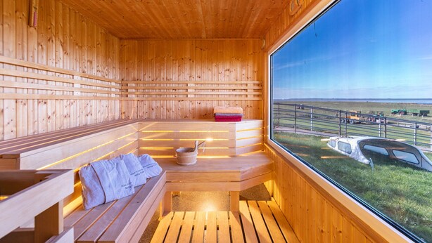 A wooden sauna with benches and a large window offering a view of the outdoors.