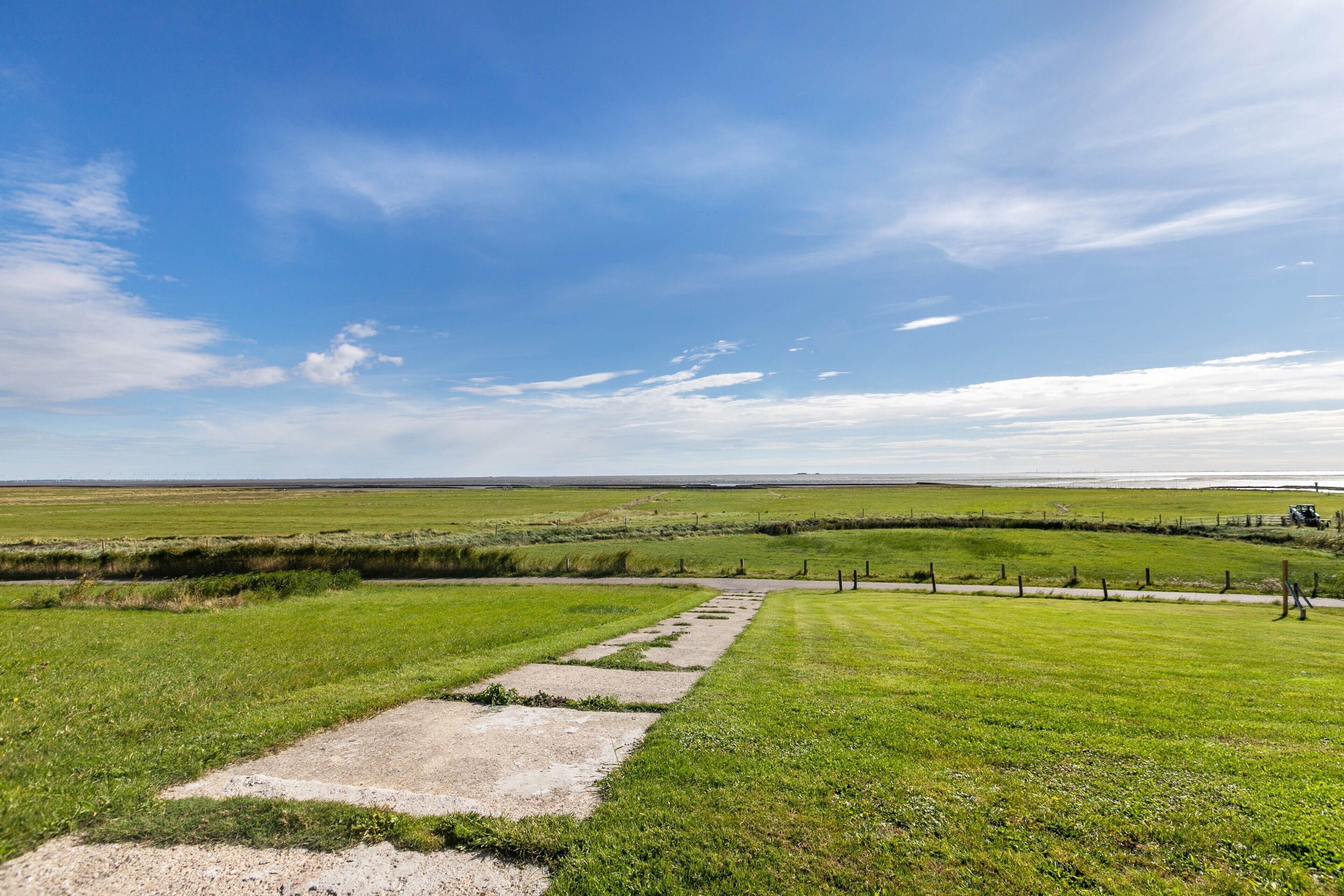 Een landelijk landschap met een onverharde weg die door velden slingert, een hek en een verre horizon.