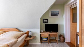A bedroom with a bed, a desk, a television, and a door.