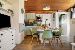 A modern kitchen with green cabinets, a dining area with two chairs, and a television on a white dresser.