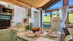 Eine Küche mit Mikrowelle, Toaster und Kaffeemaschine. Ein Esstisch ist gedeckt mit rosa Tellern, Tassen und einem Korb mit Brot.