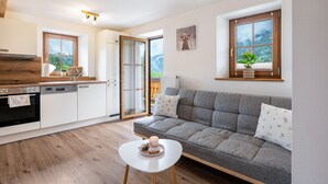 Une cuisine moderne avec un canapé gris, une petite table blanche et une vue sur l’extérieur grâce à une grande fenêtre.
