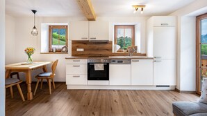 Une cuisine moderne avec des poutres en bois, des meubles blancs, un four encastré et un coin repas comprenant une table et des chaises.