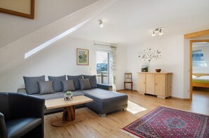 Una sala moderna con un sofá seccional gris, una mesa de centro de madera, un sillón negro, un mueble de madera y una alfombra roja con estampado.