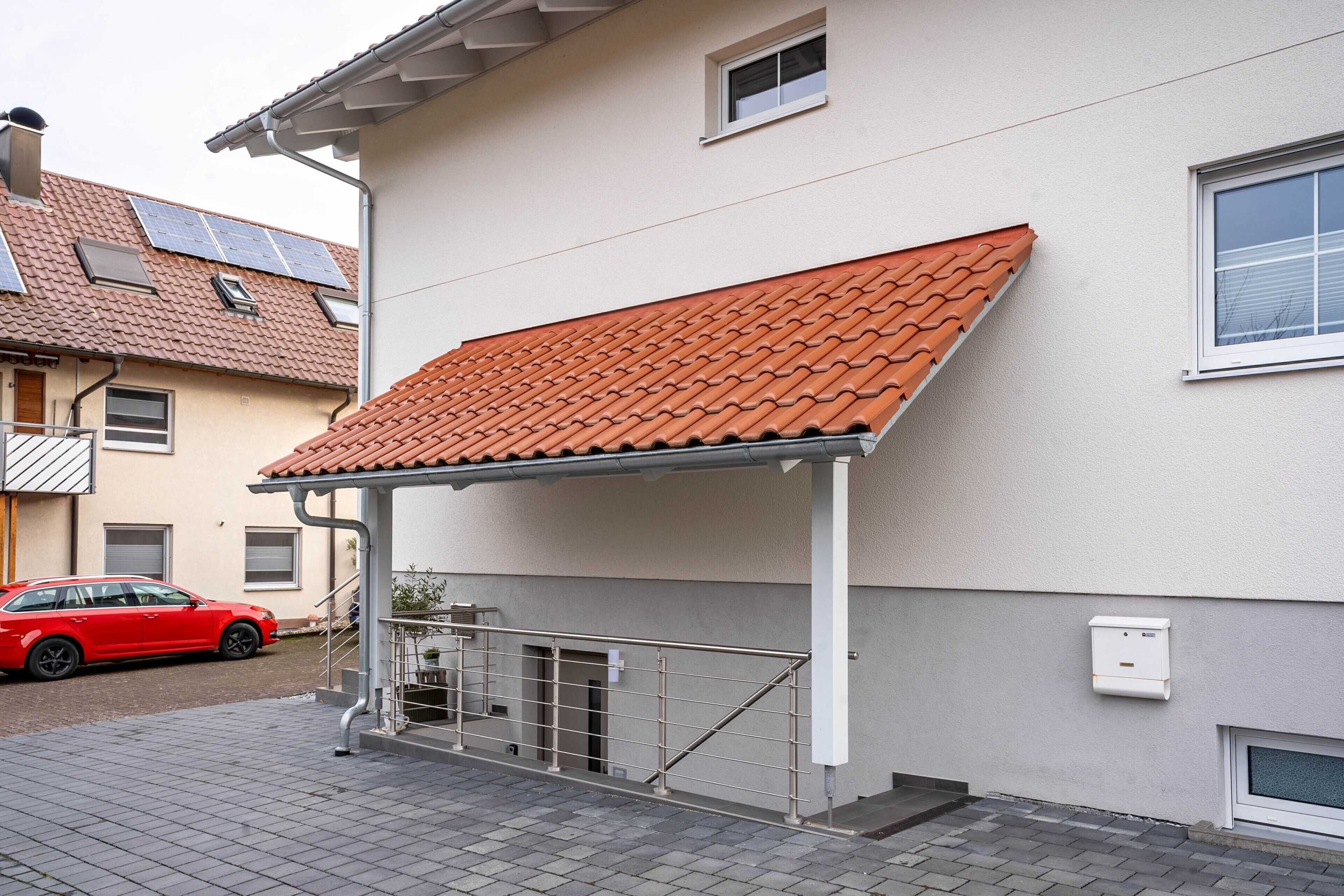 Un edificio residencial con un porche cubierto, paneles solares en el techo y un coche rojo estacionado afuera.