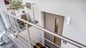 Una escalera metálica con barandilla, una puerta con picaporte vertical y una pequeña planta en maceta en el rellano.