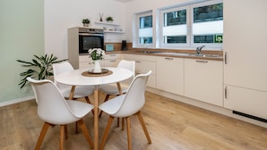 Una cocina moderna con armarios blancos, una mesa redonda con sillas blancas y una planta en maceta sobre la mesa.