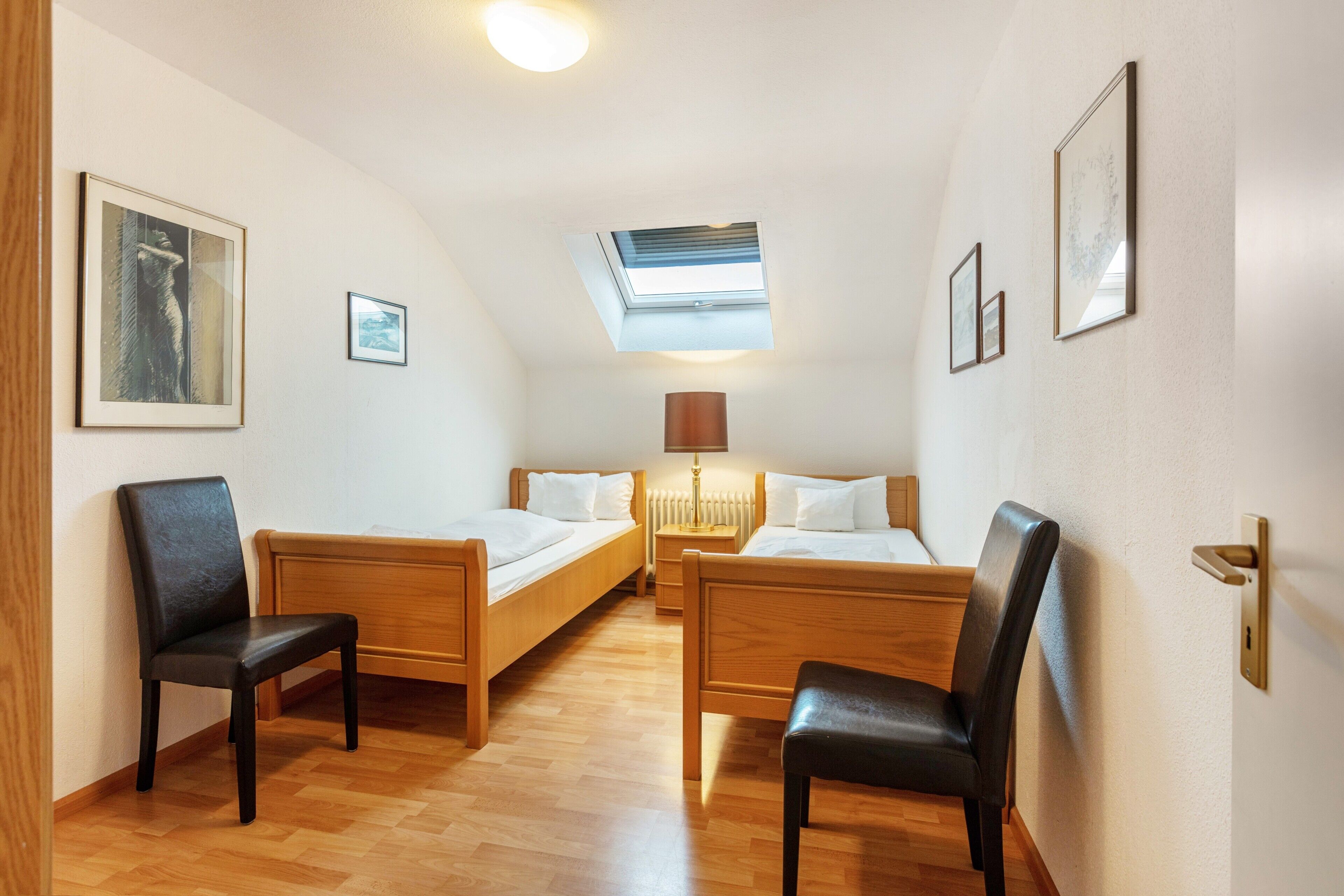 Een kamer met twee houten bedden, een plafondventilator, een dakraam en een deur met een hendel.