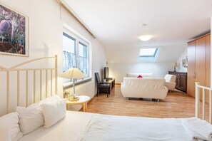 Une chambre à coucher comprenant un lit, un bureau, une chaise, un canapé, un radiateur, une fenêtre et un puits de lumière.