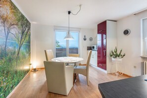 Une cuisine moderne avec des meubles de couleur rouge, un coin repas avec une table ronde et des chaises, et une vue sur un lac par une grande fenêtre.